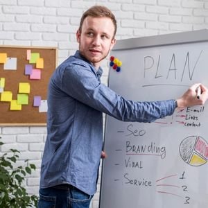 A man stands in front of a whiteboard, writing notes with a marker, focused on his task.